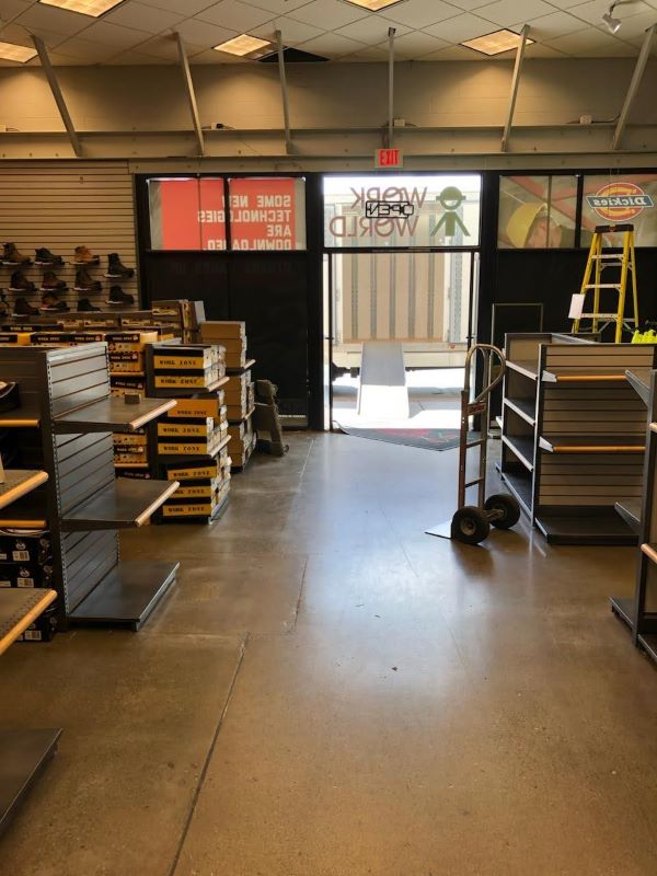 Retail store being cleared out by a professional moving company, with empty shelves, stacked boxes, a dolly, and a ramp leading to a moving truck.